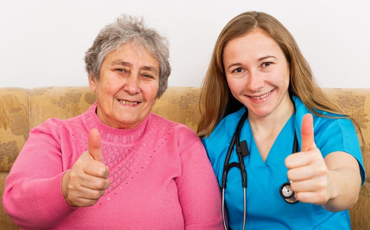 Photo of elderly woman and young caregiver showing thumbs up