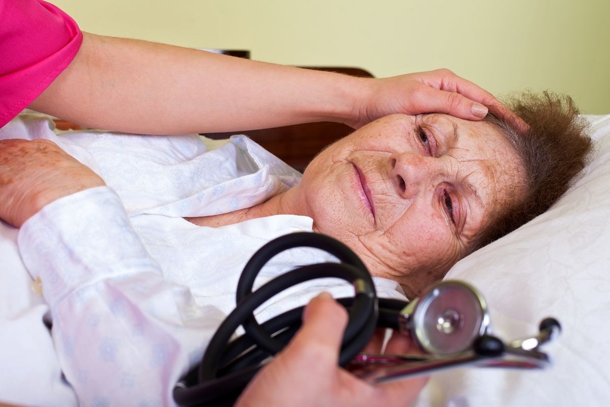 Picture of a sick elderly woman with her caregiver holding a stethoscope